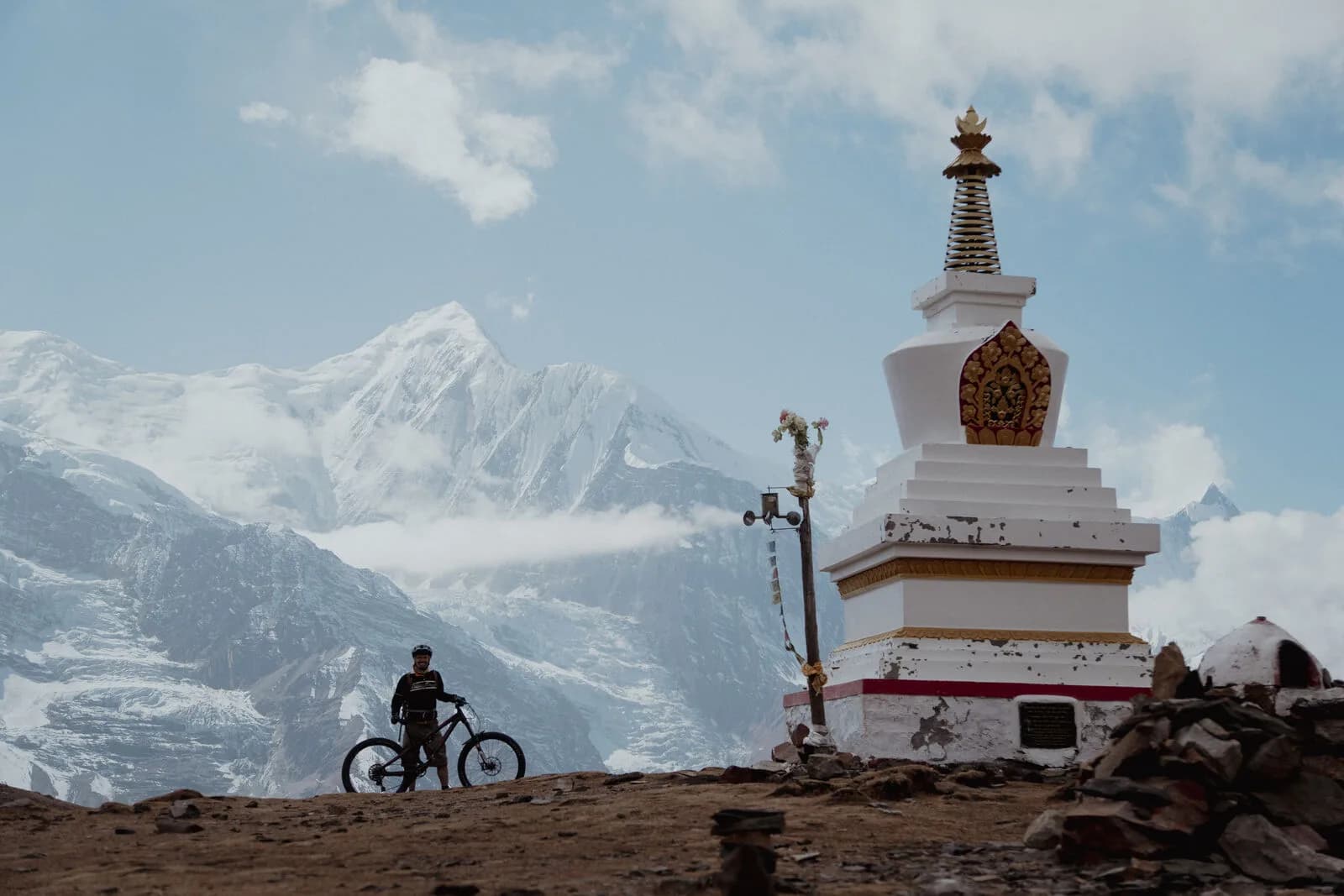 A white and gold chorten stands on brown high ground before an immense wall of snow peaks.