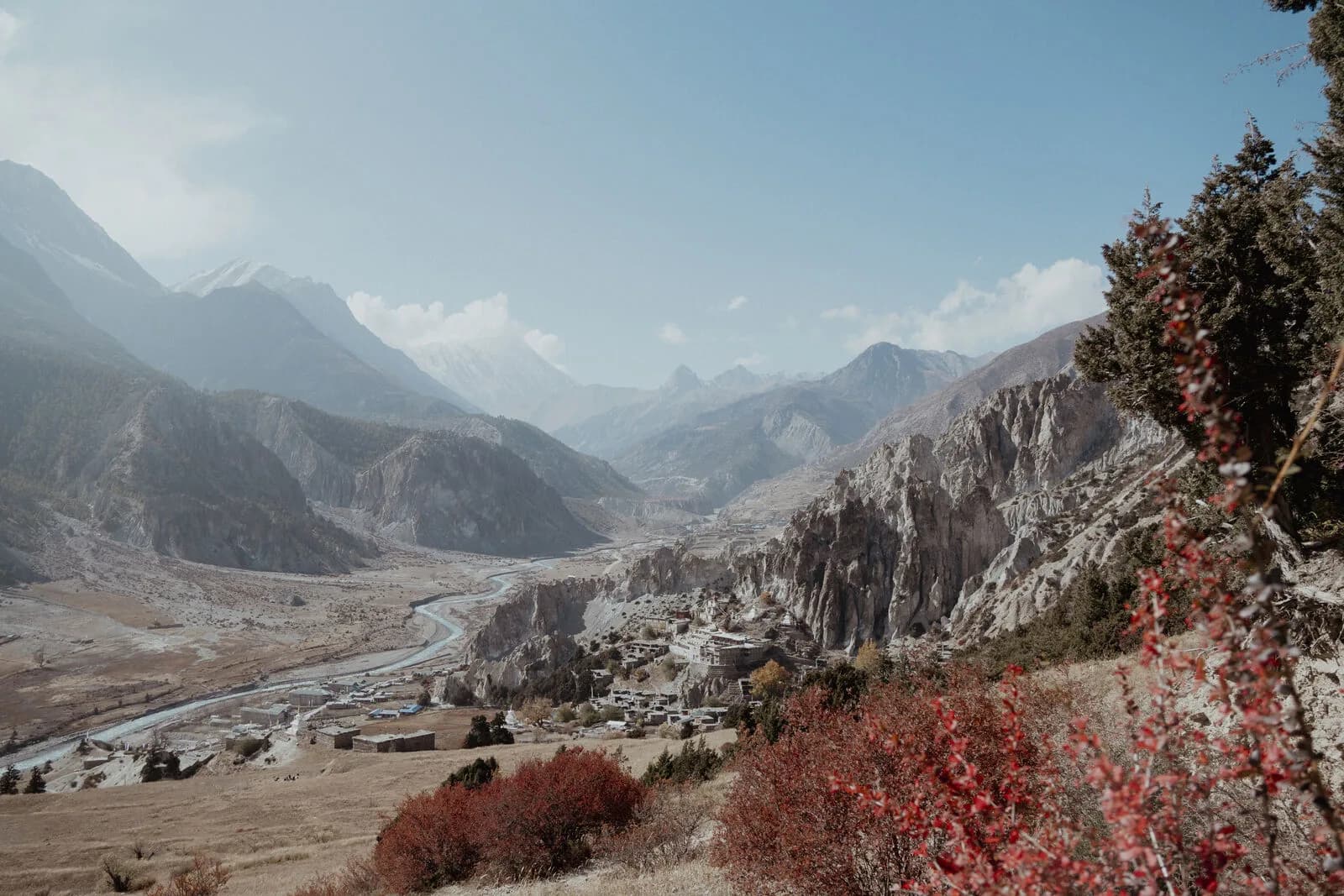 A wide mountain valley with a stone village on the far slope, autumn colour below snow ridges.