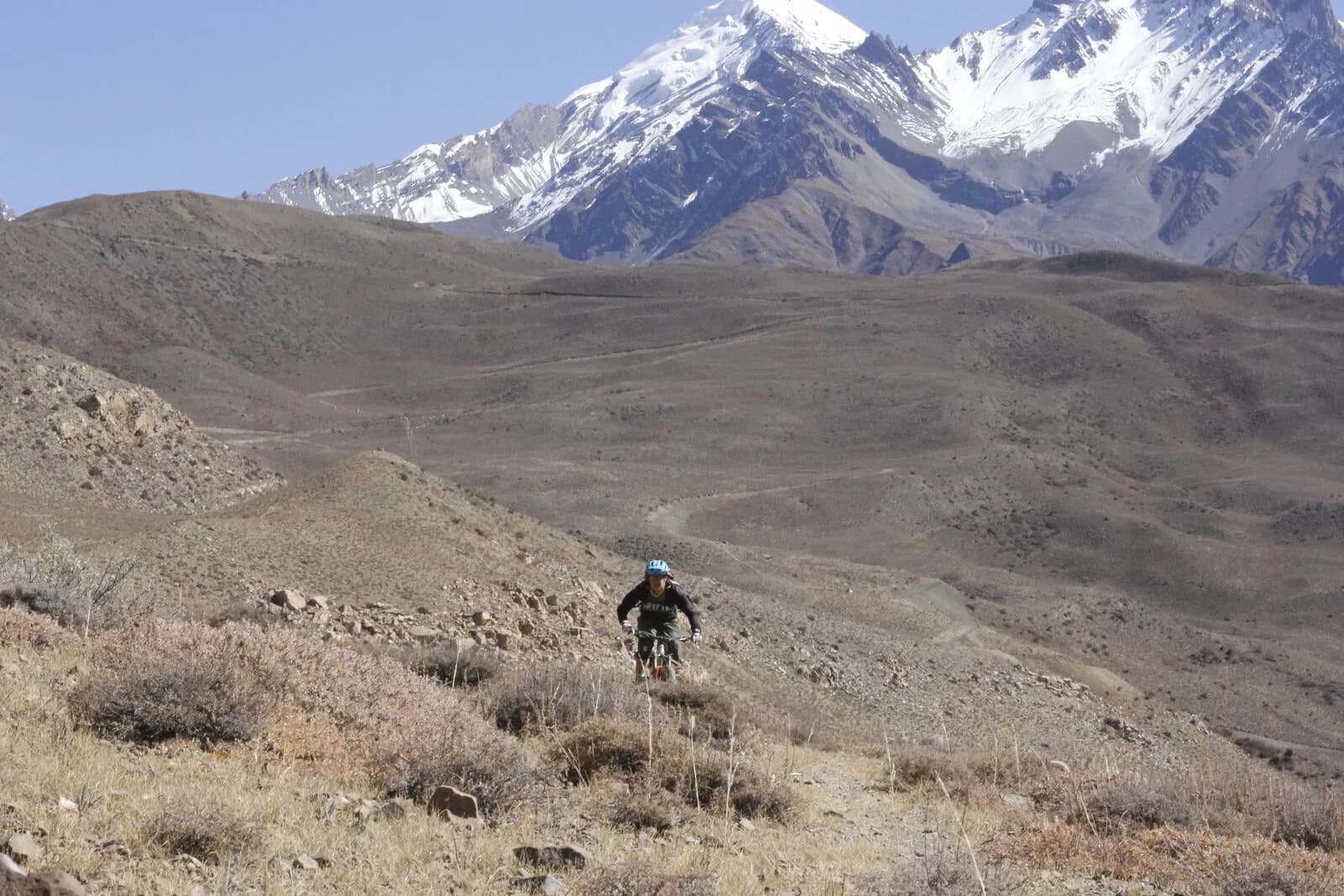 A single rider dwarfed by dry, folded mountain ranges beneath a distant snow peak.