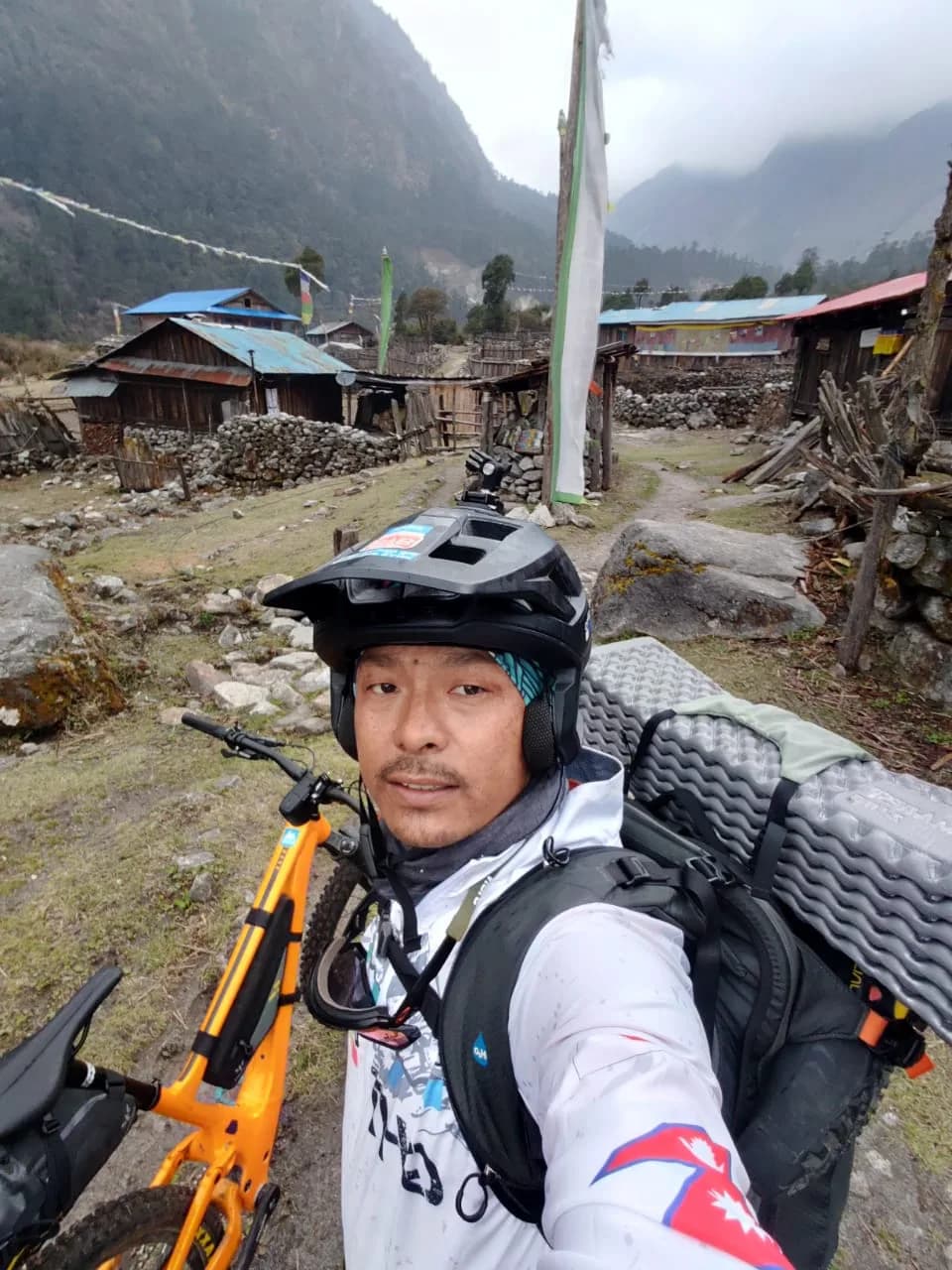 Mangal Lama in a helmet, his bike and a loaded pack beside him, in a stone village on the way to Kangchenjunga Base Camp.