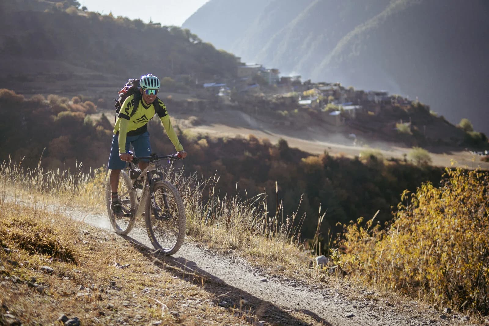 A mountain biker rides narrow singletrack through golden autumn scrub high above a river valley.